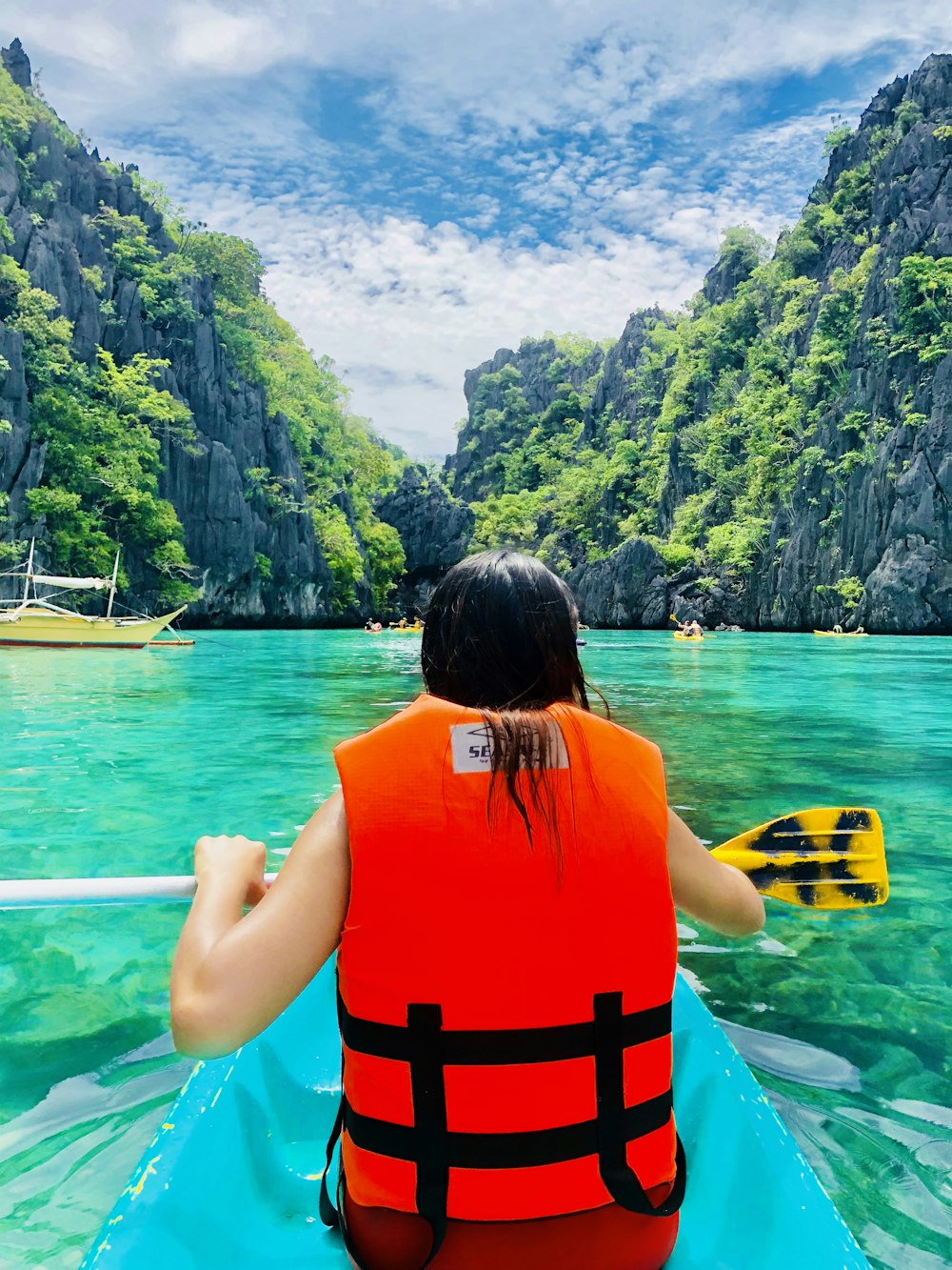 woman in orange and black life vest sitting on yellow boat on blue sea during daytime