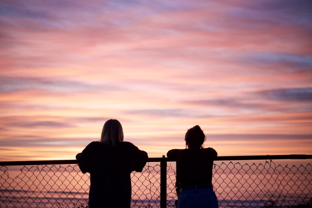 silhouette of 2 person standing beside fence during sunset