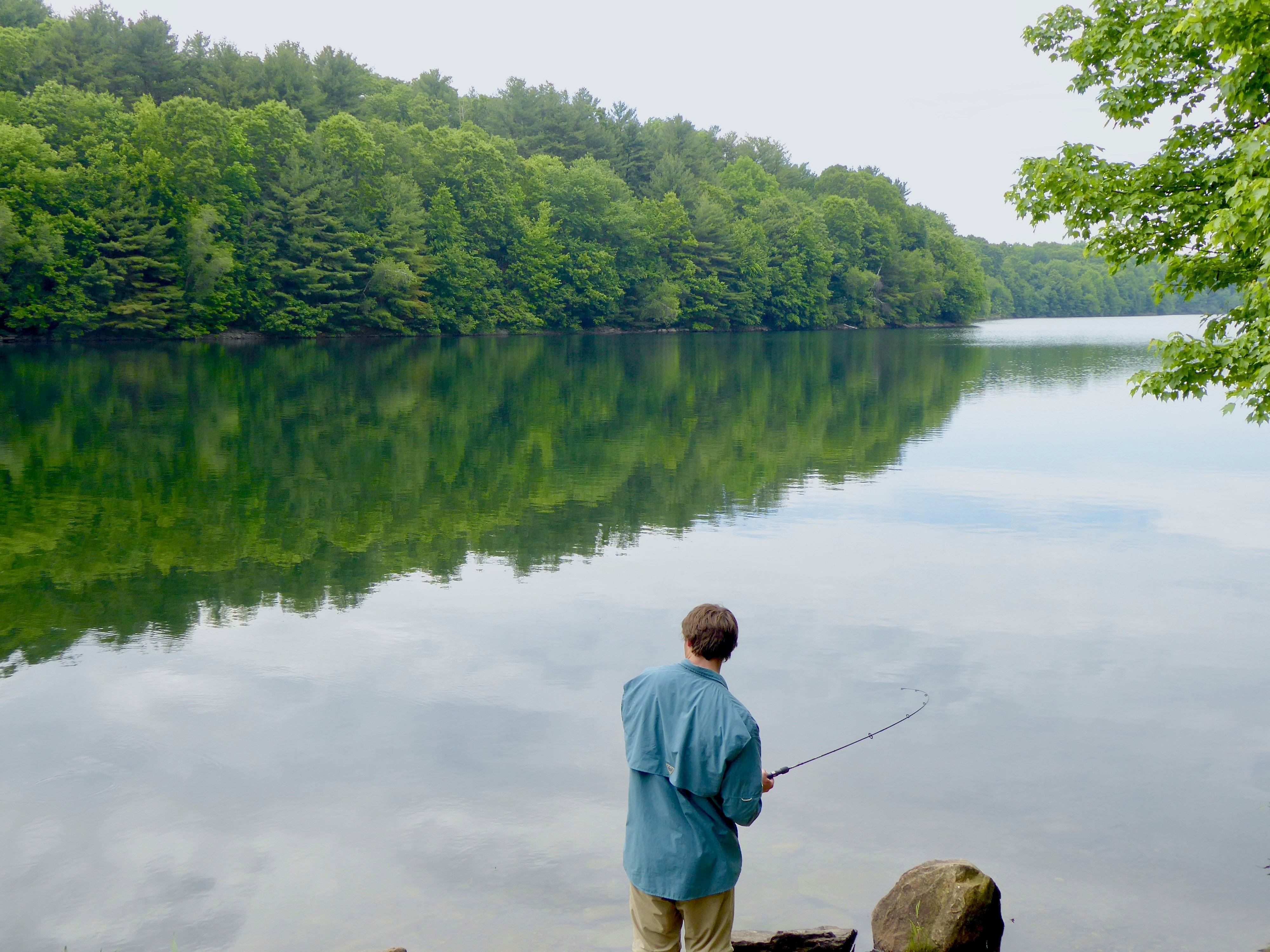 man in blue shirt fishing on lake during daytime