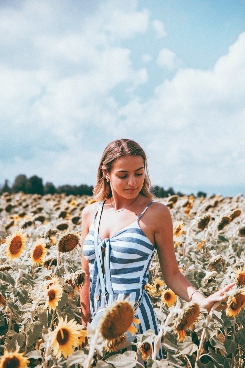 woman in white and blue spaghetti strap dress standing on brown flower field during daytime
