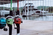 Several brightly colored fishing rods with Zebco Splash branding are mounted on a wooden dock. In the background, a large boat is docked in a marina, with green hills visible across the water.