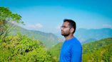 man in blue crew neck shirt wearing black framed eyeglasses standing near green plants during daytime