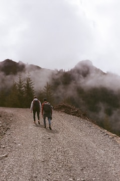 3 people walking on dirt road near foggy mountain during daytime