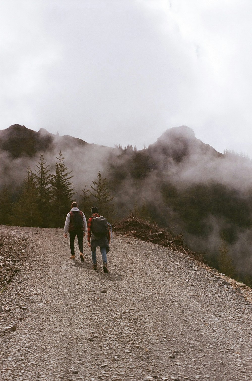 3 people walking on dirt road near foggy mountain during daytime