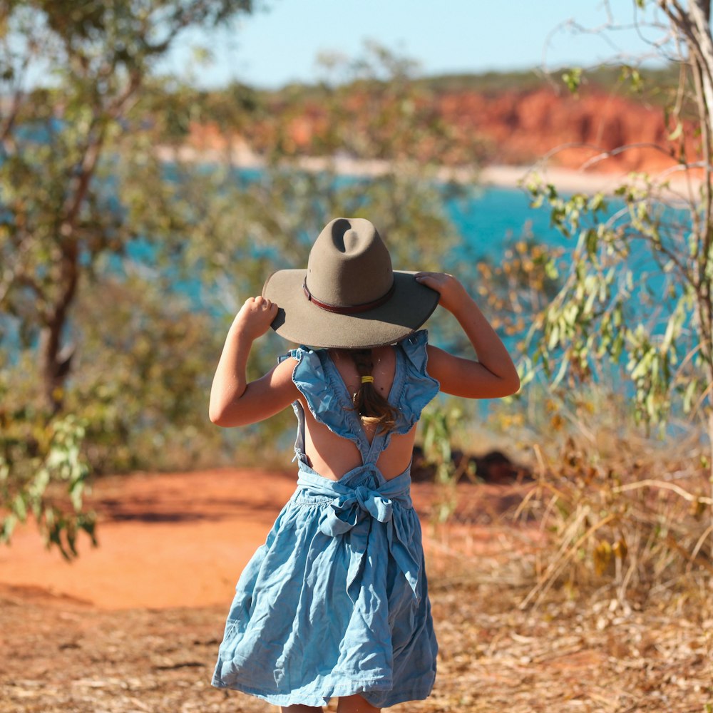 woman in blue and white dress wearing white fedora hat standing on brown field during daytime