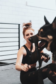 woman in black tank top holding black and tan short coat medium dog