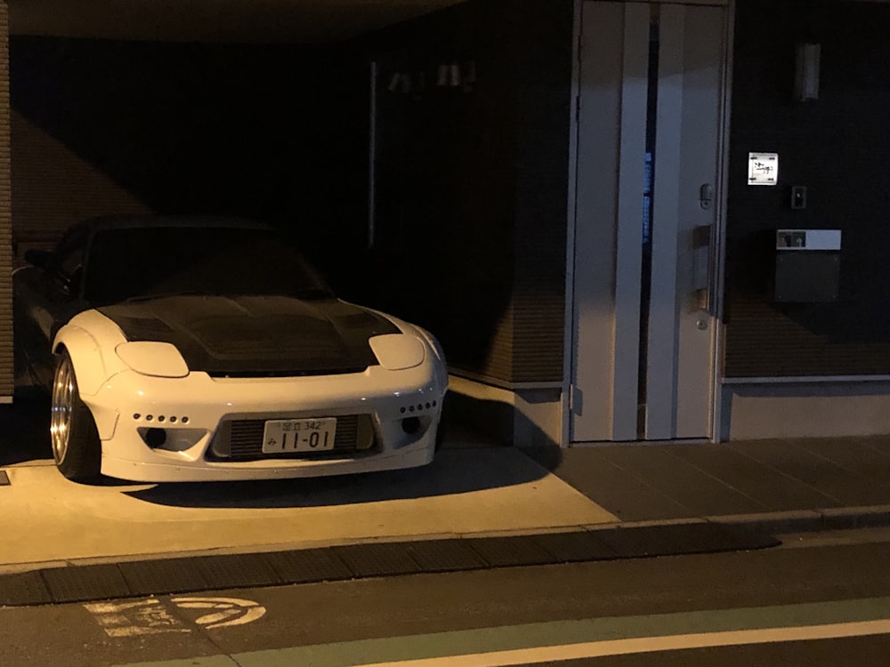 white porsche 911 parked in front of gray metal door