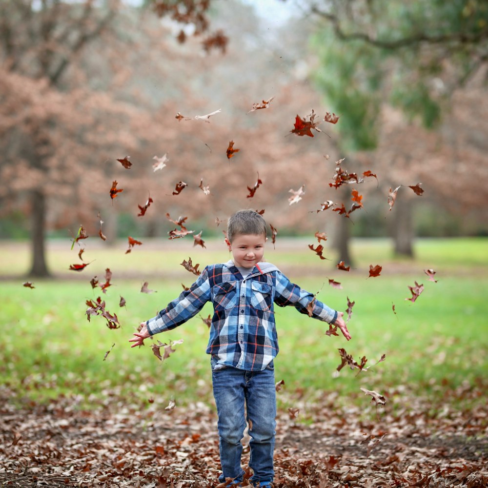 boy in blue and white plaid dress shirt and blue denim jeans standing on dried leaves