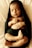 A peacefully sleeping baby wrapped in a dark green blanket. The baby is lying on its back with eyes closed and hands gently folded over its chest. The blanket partially covers the baby's body, and the background appears to be a soft, light-colored surface.