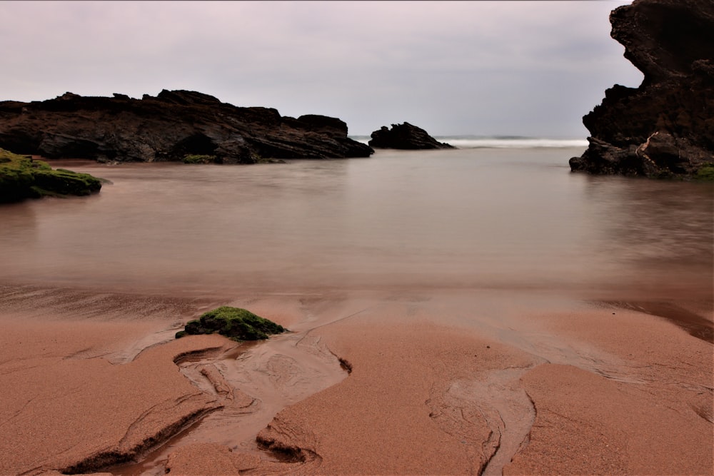 brown sand beach with green moss and brown rock formation