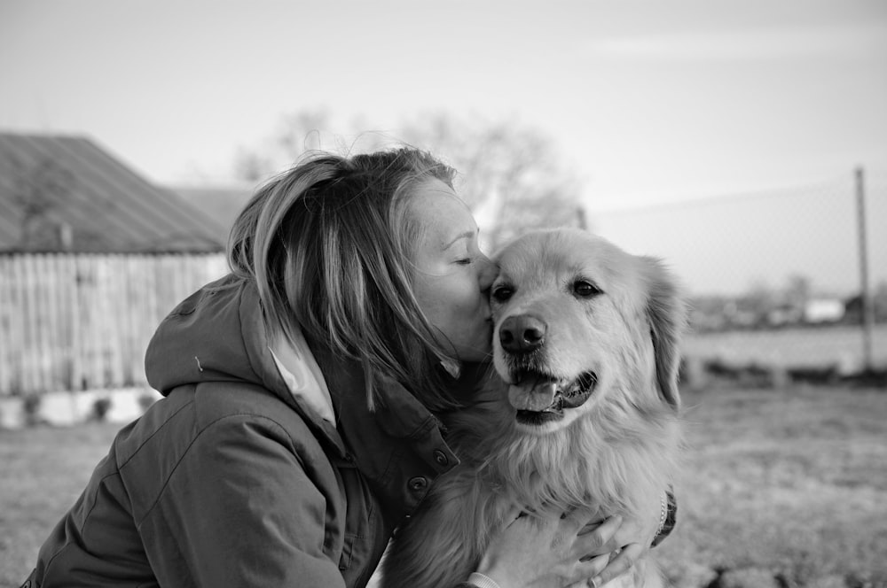 Foto en escala de grises de mujer besando golden retriever