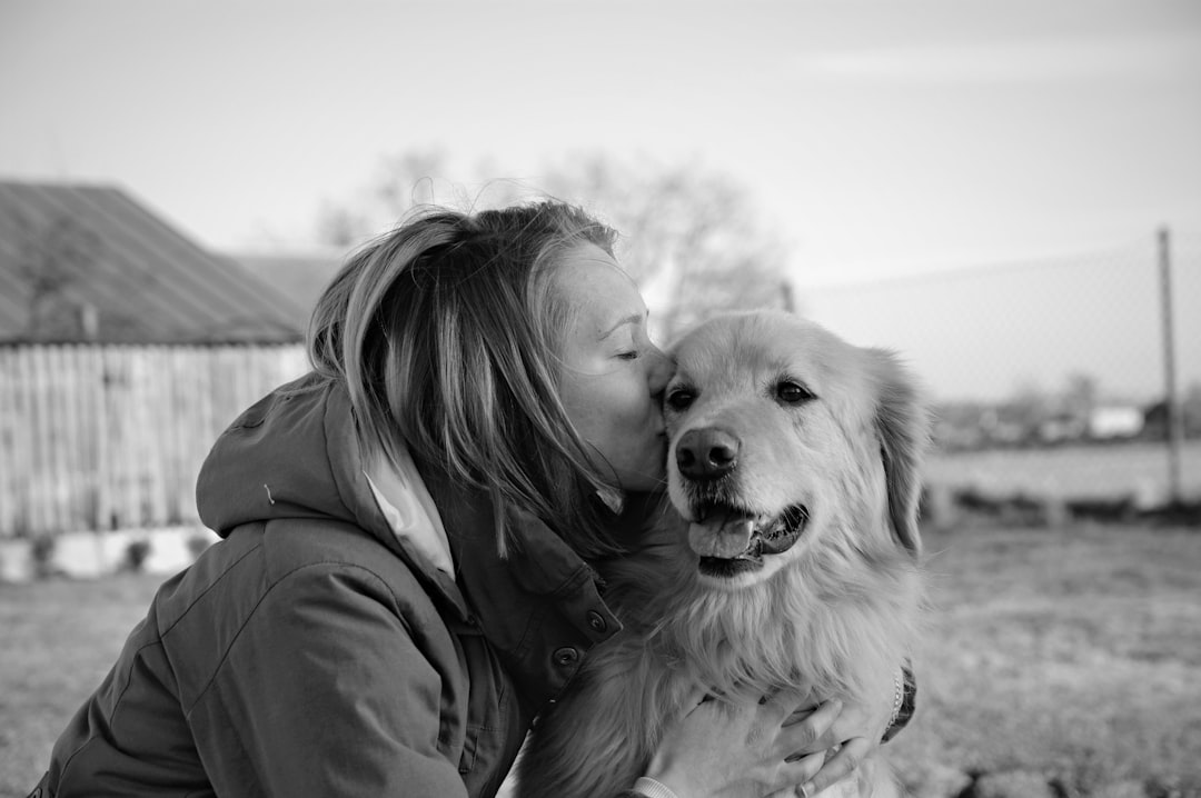grayscale photo of woman kissing golden retriever
