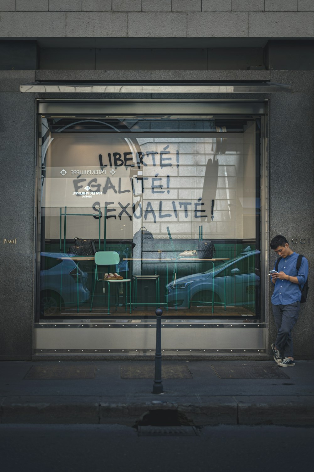 man in blue dress shirt and blue denim jeans standing in front of glass window