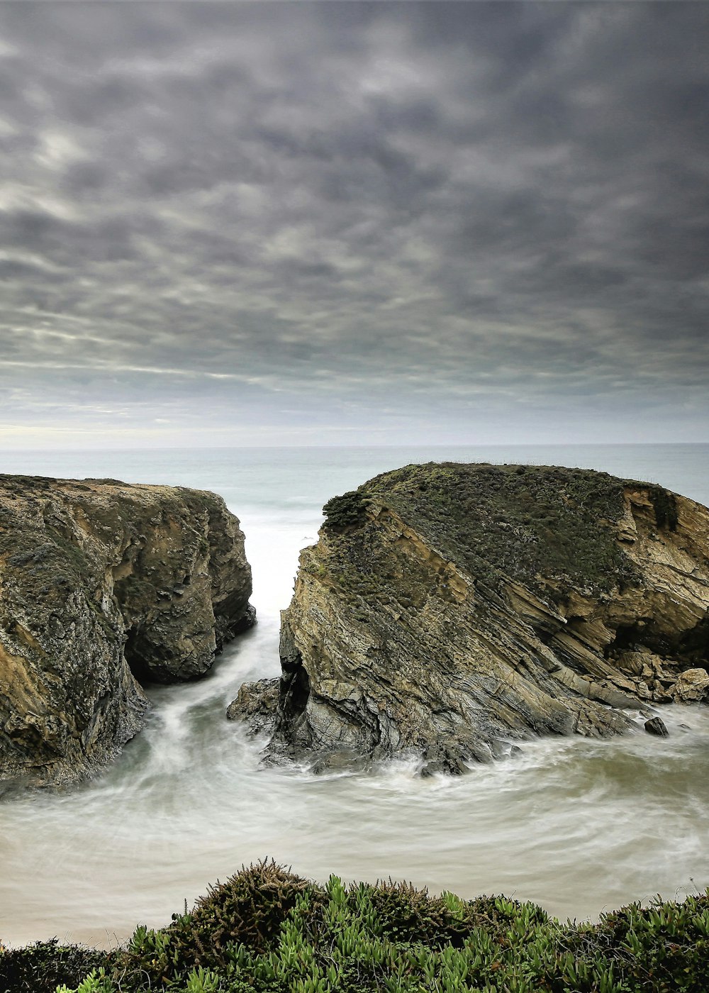 brown rock formation on sea under gray clouds