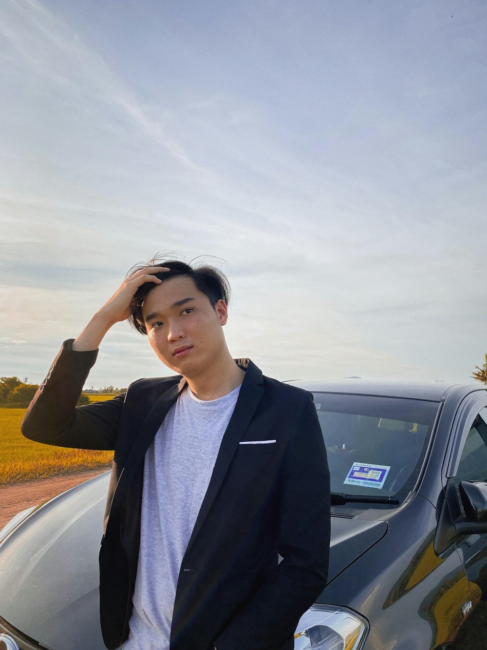 man in black blazer standing beside black car during daytime