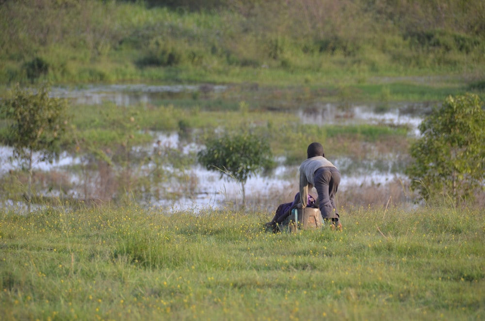 man in blue shirt sitting on green grass field near lake during daytime