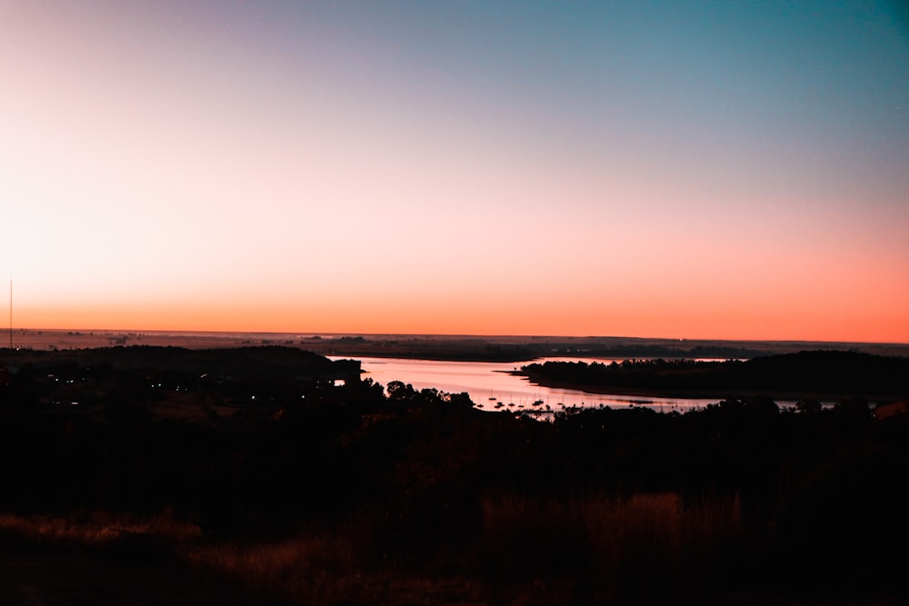 body of water near green trees during sunset