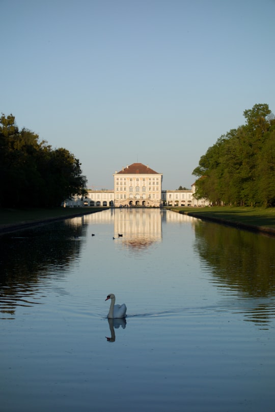 brown and white concrete building near green trees and river during daytime in Schlosspark Nymphenburg Germany