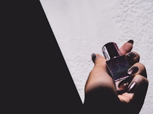 Hand holding a small bottle of nail polish with soft-focus salon background.