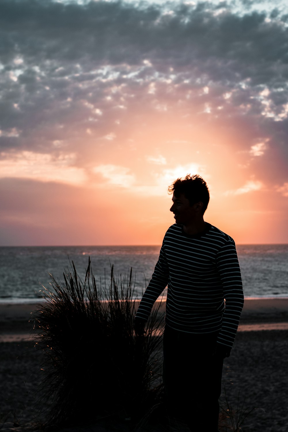man in black and white striped long sleeve shirt standing near sea during sunset