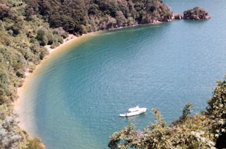 A serene turquoise bay with a small boat anchored near a lush tropical island shore.