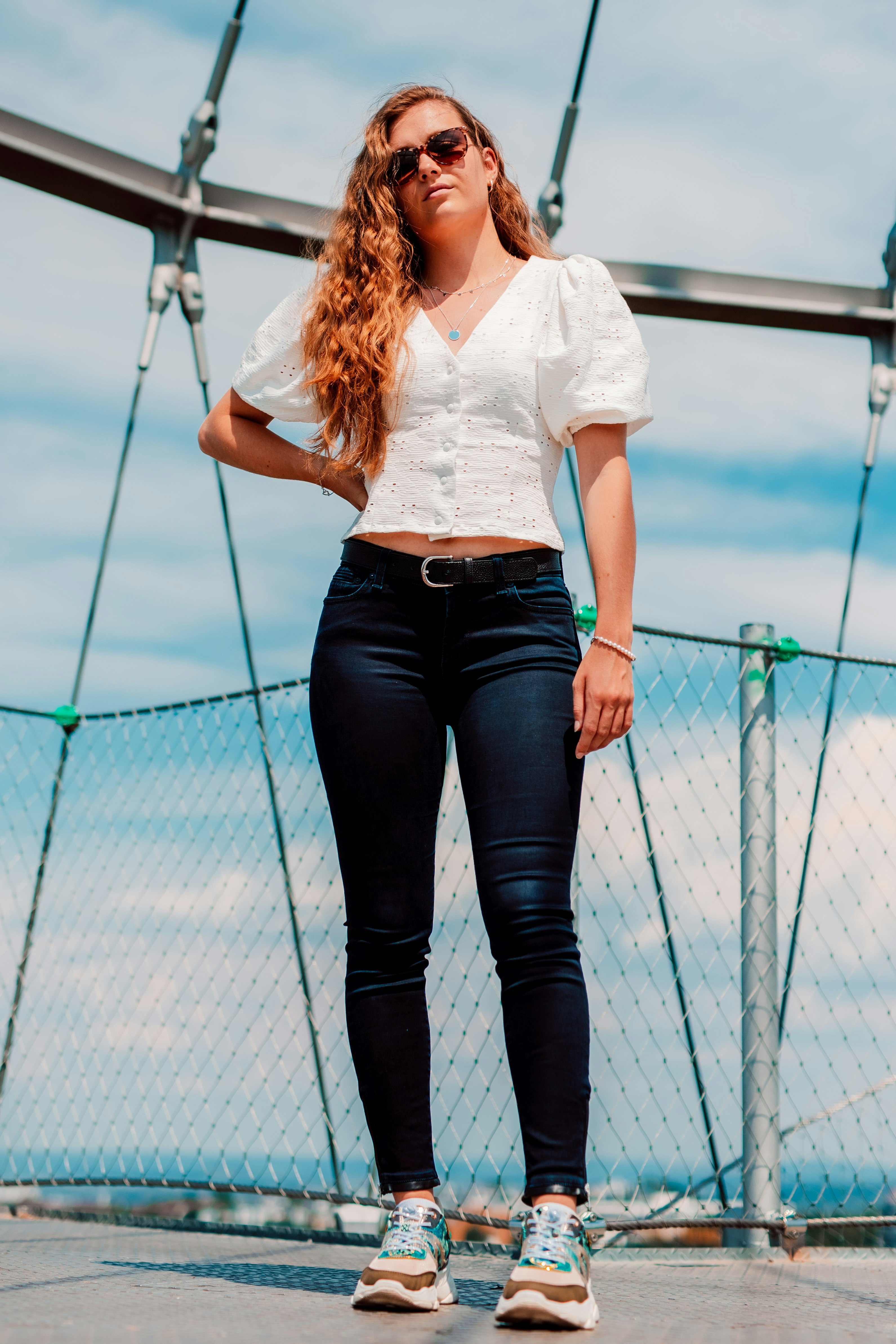 woman in white shirt and black denim jeans standing on blue metal bridge during daytime