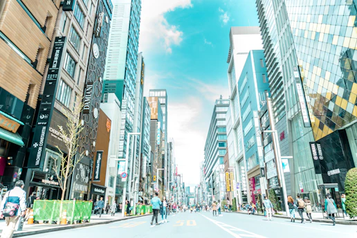 A vibrant city street bustling with diverse businesses and lively pedestrians under a bright sky.