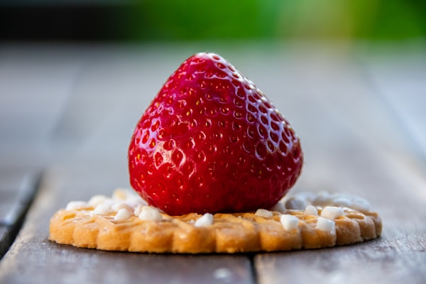 A strawberry sitting on top of a cracker on a wooden table