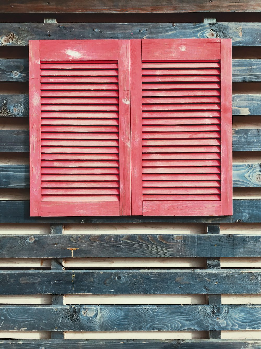 a red shuttered window on a wooden wall