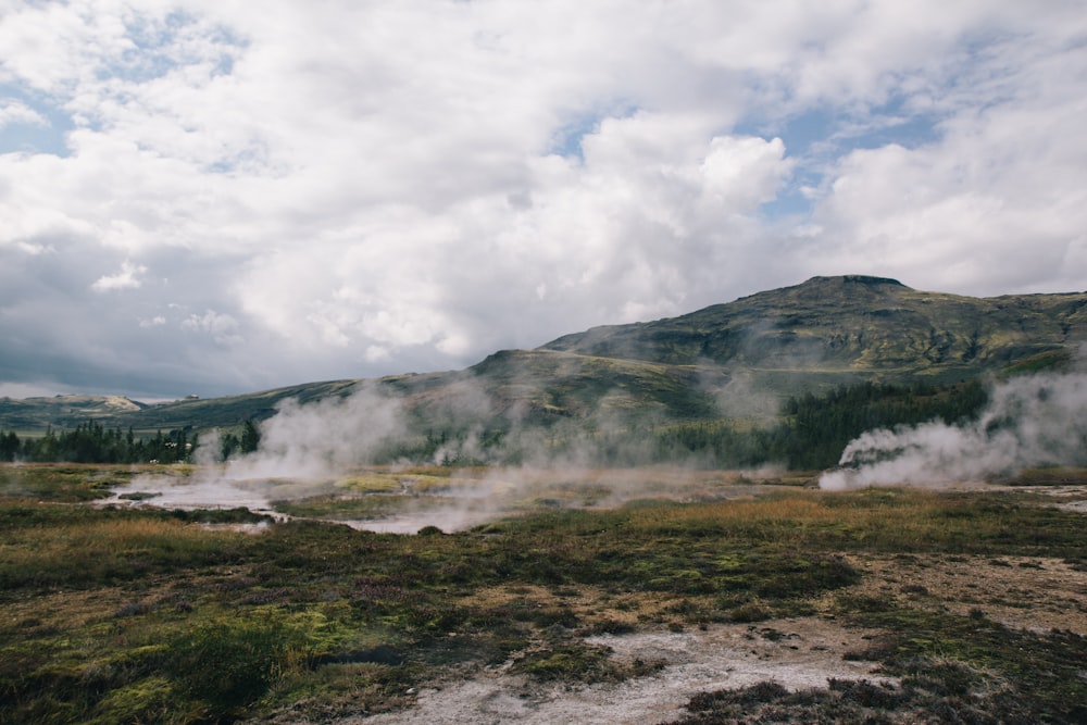 steam rises from the ground in front of a mountain