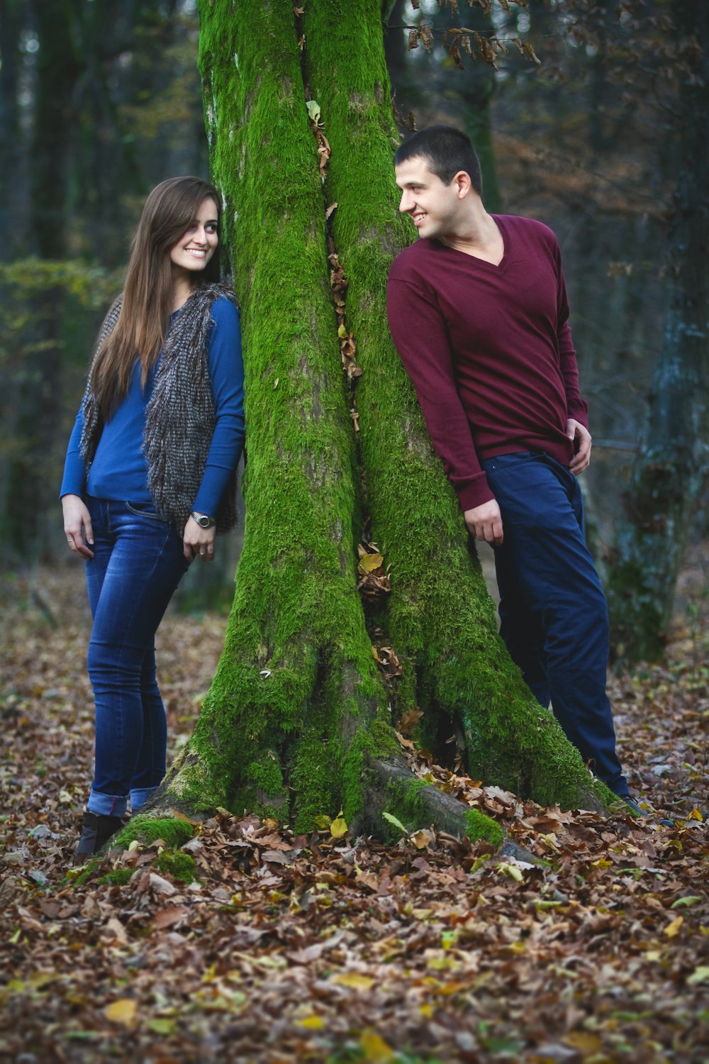 woman in maroon long sleeve shirt and blue denim jeans standing beside green moss covered tree