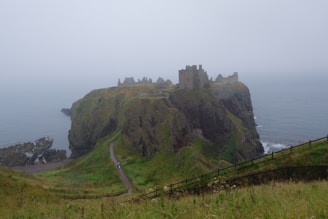 A misty morning view of old Scottish castle ruins perched on a rocky cliff overlooking the sea.