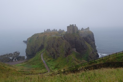 A misty morning view of old Scottish castle ruins perched on a rocky cliff overlooking the sea.