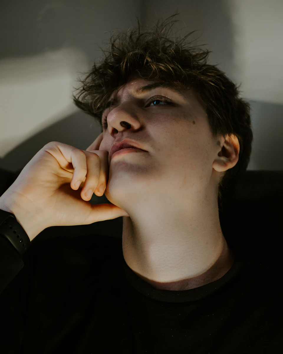 Young man rests chin on hand with eyes closed in contemplative pose outdoors