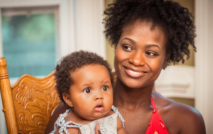 woman in orange shirt carrying baby in white and blue floral shirt