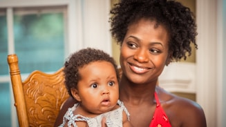 woman in orange shirt carrying baby in white and blue floral shirt