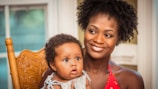 woman in orange shirt carrying baby in white and blue floral shirt