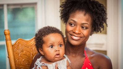 woman in orange shirt carrying baby in white and blue floral shirt