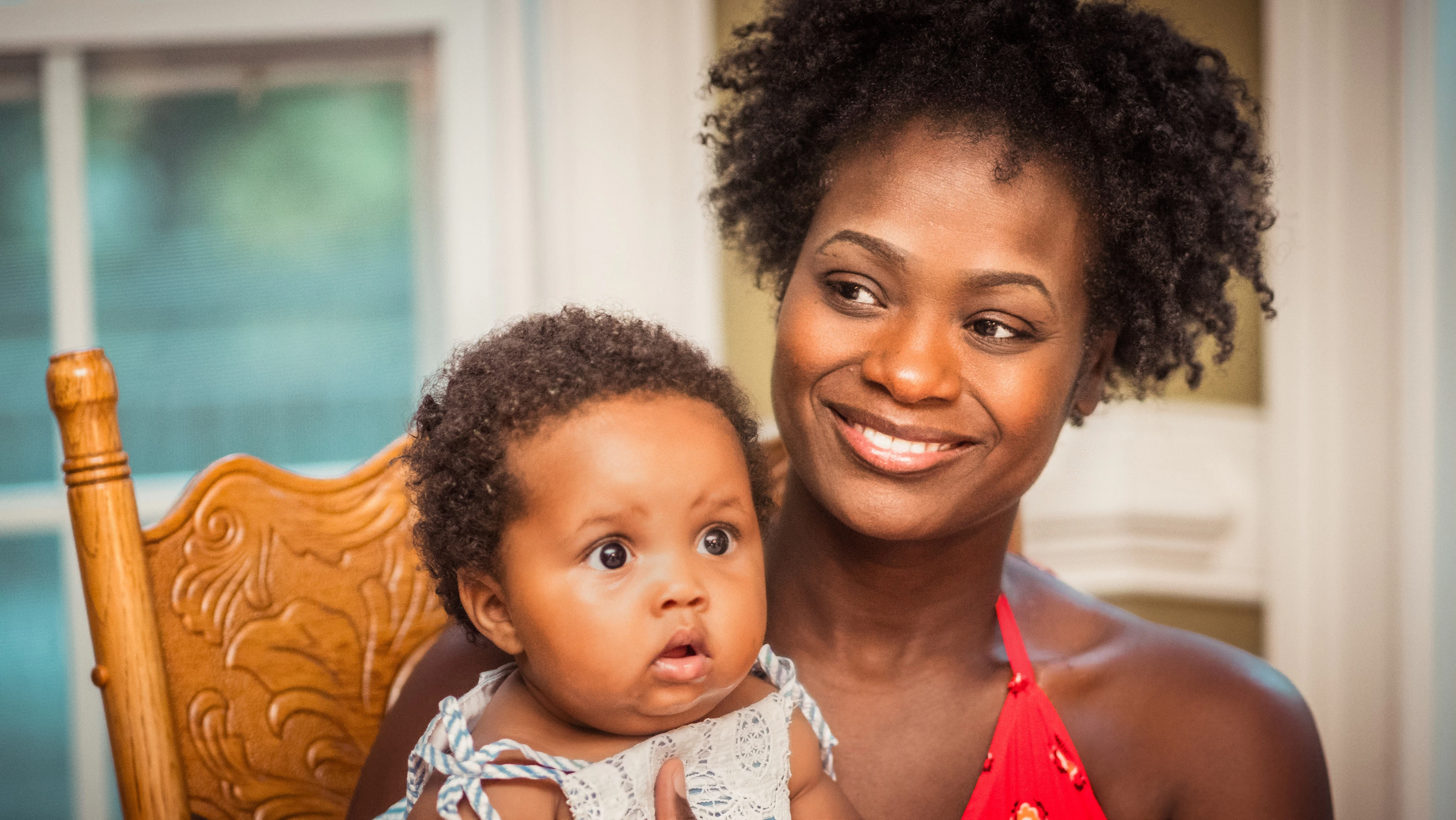A woman in an orange shirt holding a baby against her shoulder