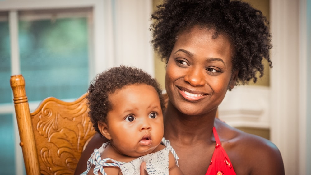 woman in orange shirt carrying baby in white and blue floral shirt