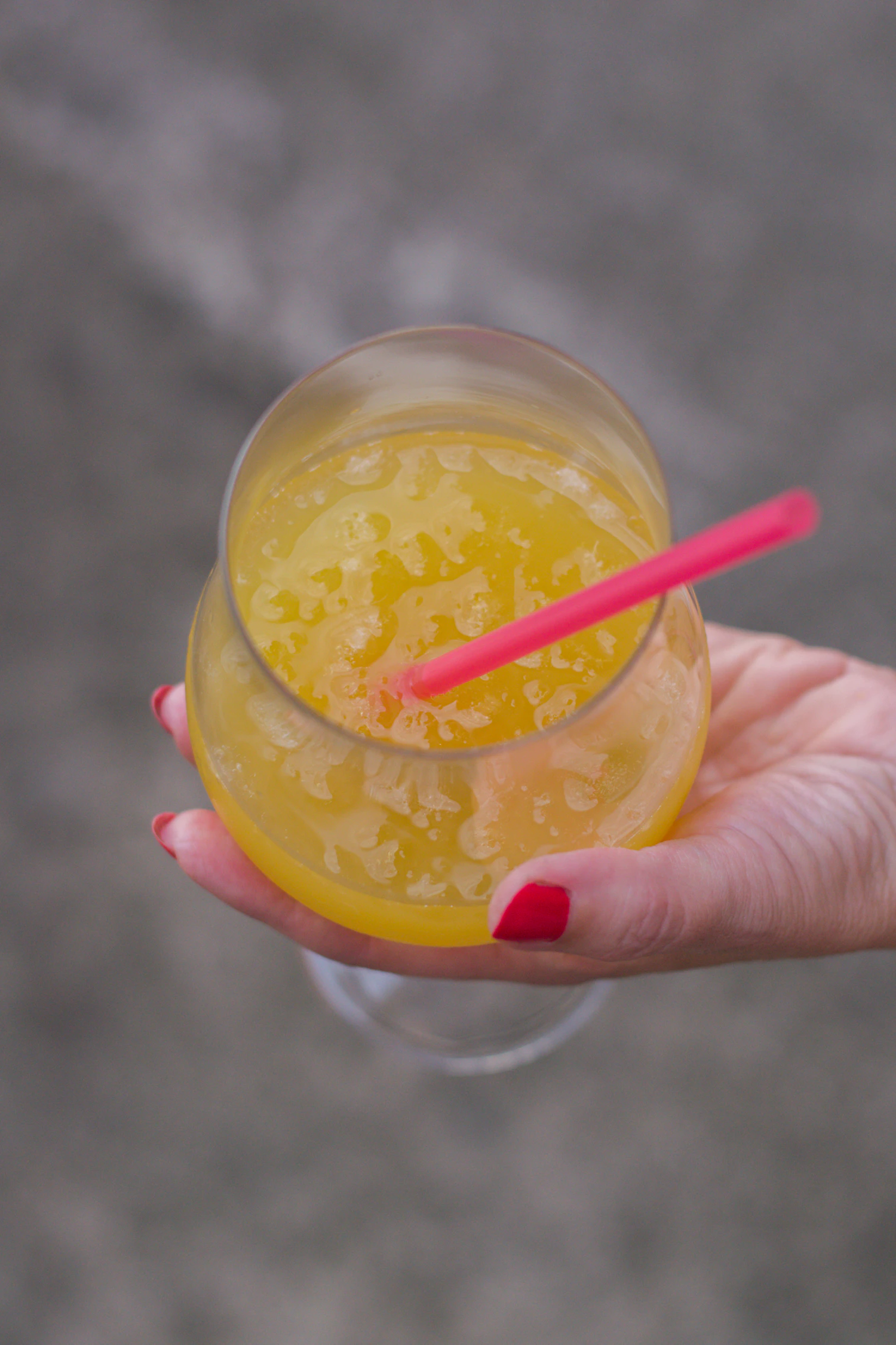 A hand holding a glass of yellow mango drink with a pink straw