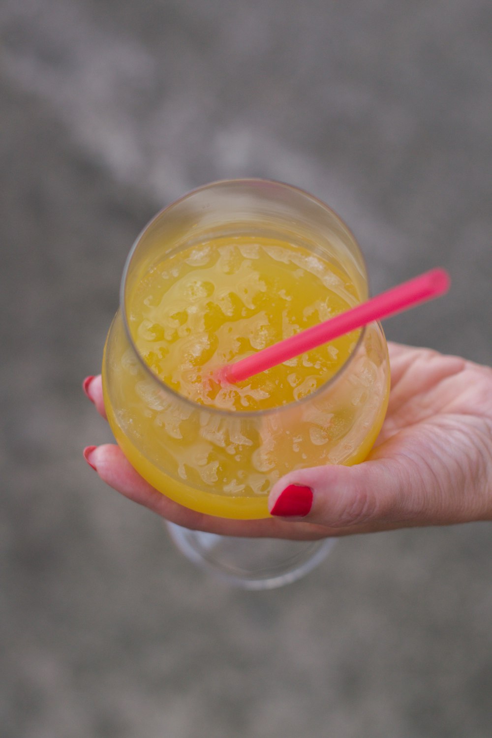 person holding clear plastic cup with orange liquid