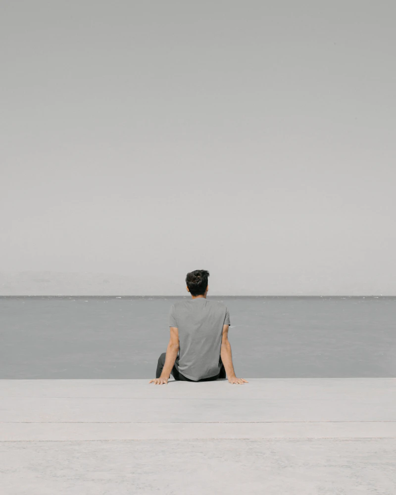 Hombre sentado en la arena mirando el agua: descanso y calma