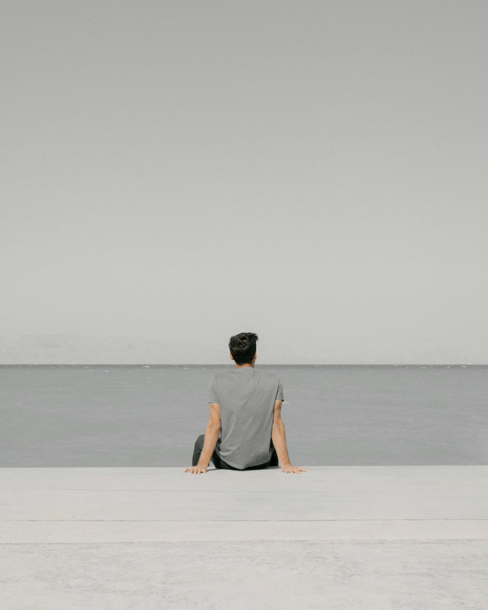 man in yellow shirt and black shorts sitting on white sand near body of water during