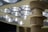 A close-up view of an overhead surgical light with multiple LED bulbs. The image focuses on the fixture's central column and the lights, which emit a bright white glow.