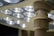 A close-up view of an overhead surgical light with multiple LED bulbs. The image focuses on the fixture's central column and the lights, which emit a bright white glow.
