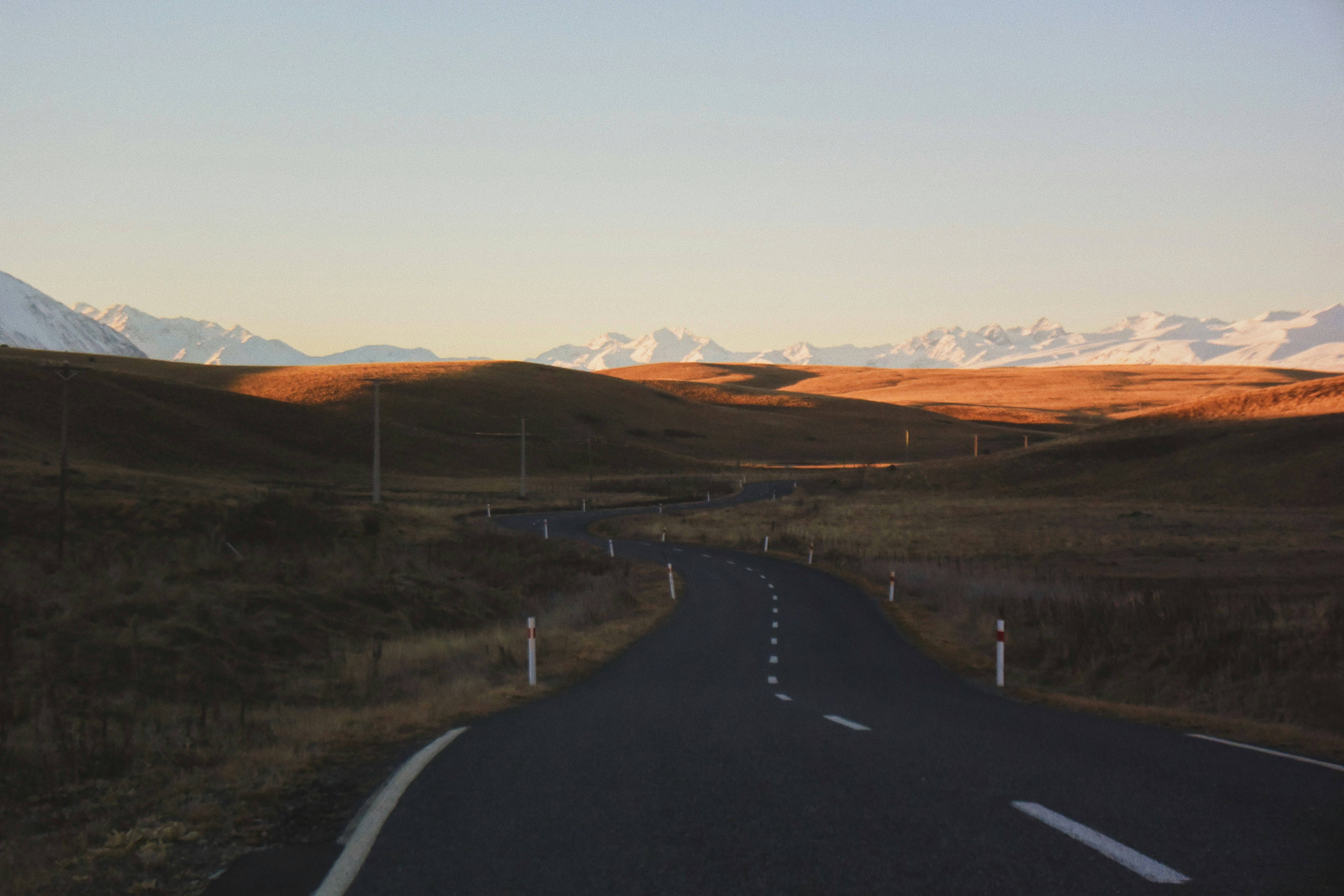 black asphalt road in between brown grass field during daytime