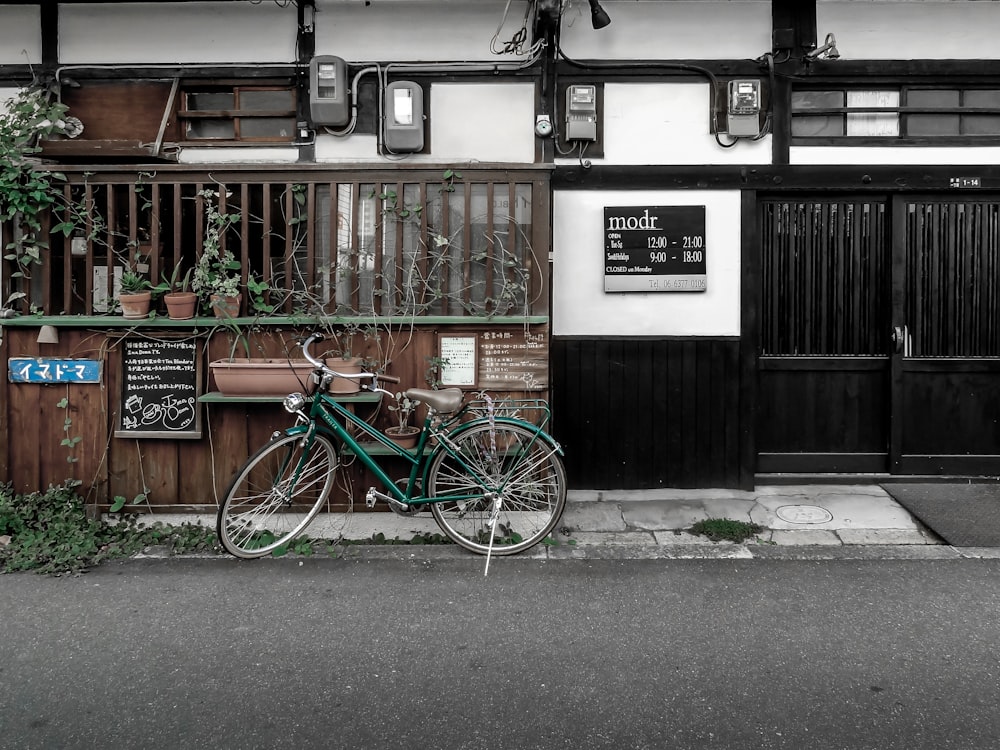 blue and green bicycle parked beside brown wooden house during daytime