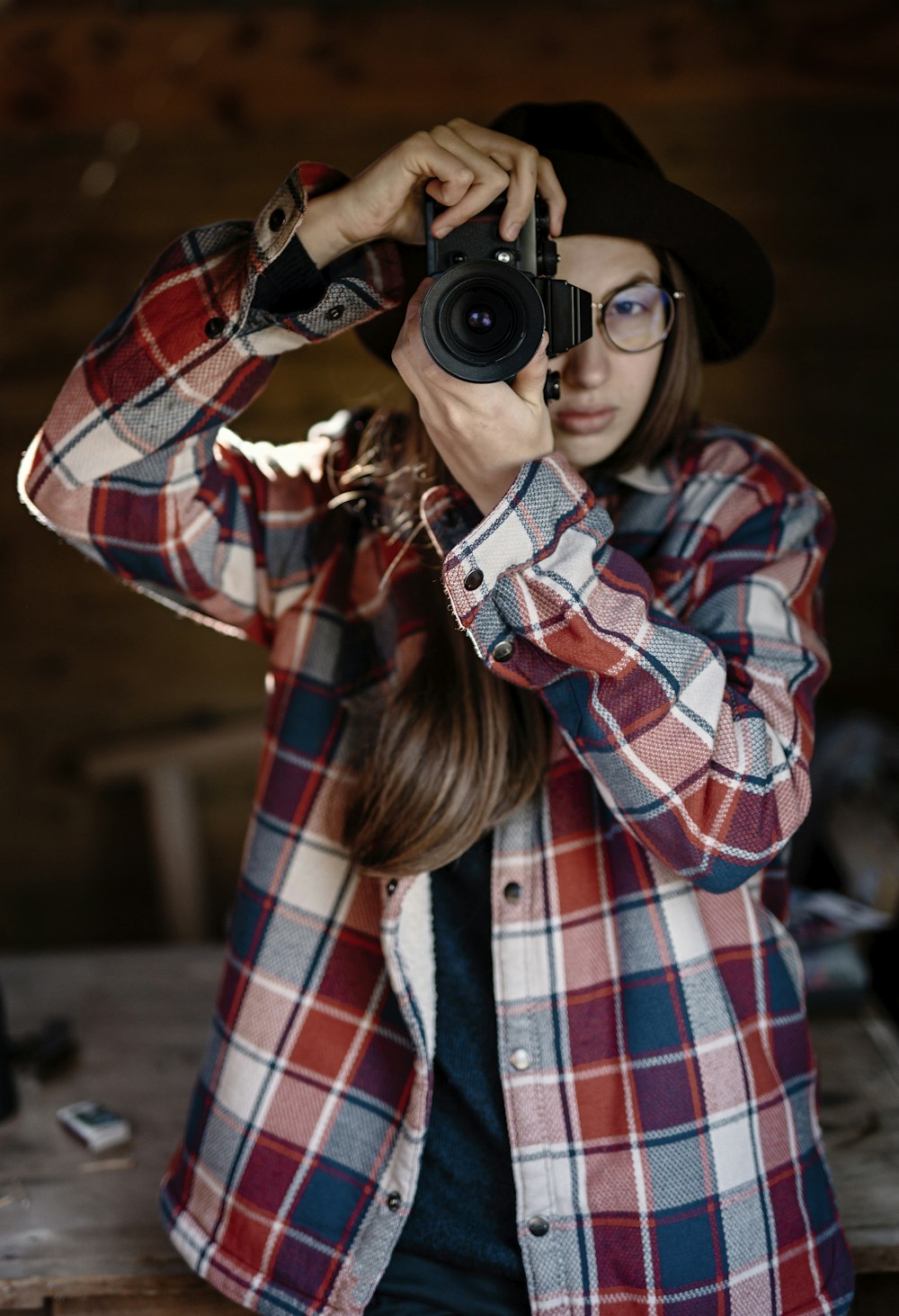 黒のデジタル一眼レフカメラを持つ赤、白、黒の格子縞のドレスシャツを着た女性