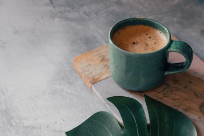 Close-up of a steaming cup of Costa Rican coffee on a wooden table surrounded by tropical leaves.